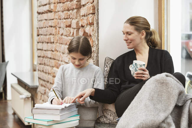 Sorridente donna d'affari aiutare figlia mentre si studia a casa — Foto stock
