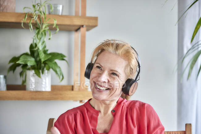 Nachdenkliche Frau mit Kopfhörern lächelt zu Hause — Stockfoto