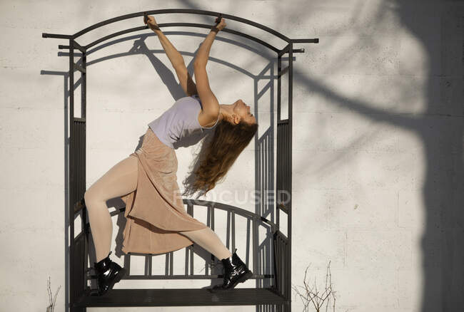 Молодая женщина танцует на металлической конструкции перед белой стеной — стоковое фото