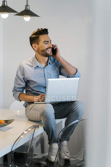 Geschäftsmann telefoniert mit Handy, während er zu Hause am Tisch sitzt — Stockfoto