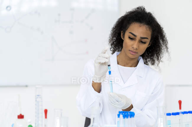 Joven investigador inyectando líquido en tubo de ensayo mientras trabaja en laboratorio - foto de stock