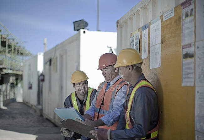 Sonrientes trabajadores de la construcción discutiendo en el sitio de construcción - foto de stock