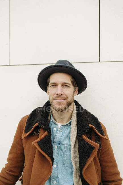 Hombre hipster abrigo y sombrero contra pared — Feliz, Color: - Photo |