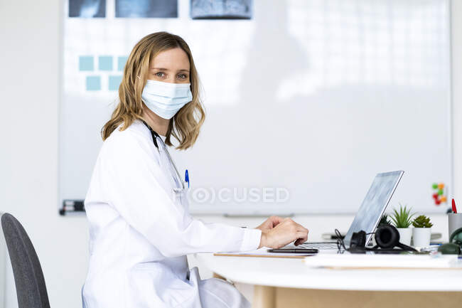 Female doctor with colleagues discussing in meeting through video call at medical clinic during COVID-19 — Stock Photo