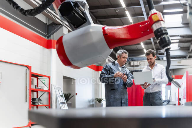 Entrepreneurs masculins avec ordinateur portable vu à travers la robotique dans l'usine — Photo de stock
