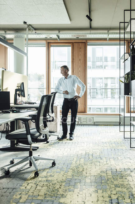 Чоловічий підприємець з рукою на стегні спираючись на крісло в офісі — стокове фото