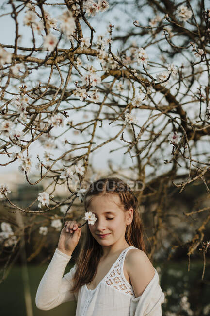 Jolie fille couvrant oeil de la branche de fleur d'amandier pendant le printemps — Photo de stock