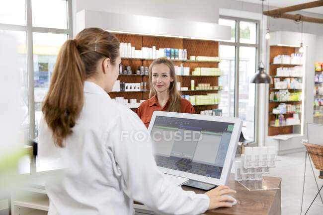 Female pharmacist using computer while customer standing at checkout in store — Stock Photo
