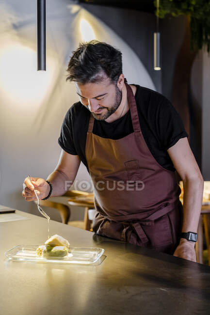 Smiling mature chef pouring liquid on food at commercial kitchen — Stock Photo