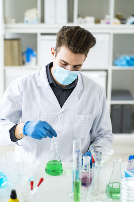 Мужской ученый смешивает жидкость во фляжке в лаборатории во время COVID-19 — стоковое фото