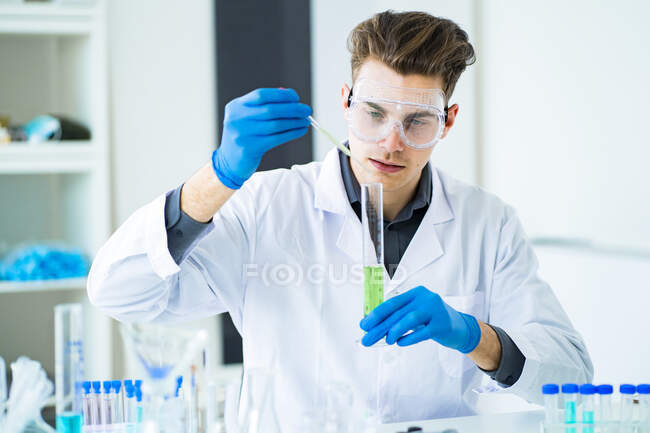 Científico joven mezclando productos químicos en cilindro graduado en laboratorio - foto de stock