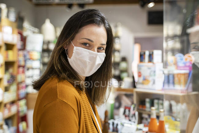 Молодая женщина в защитной маске стоит в продуктовом магазине во время пандемии — стоковое фото