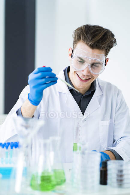 Усміхаючись, самець учений тримає піпетт під час роботи в лабораторії. — стокове фото