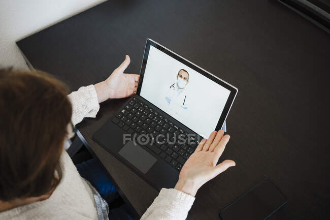 Старша жінка з ноутбуком обговорює з лікарем через відеодзвінок за столом — стокове фото