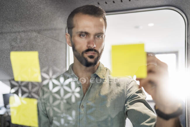 Professional putting adhesive note on telephone booth glass at office — Stock Photo