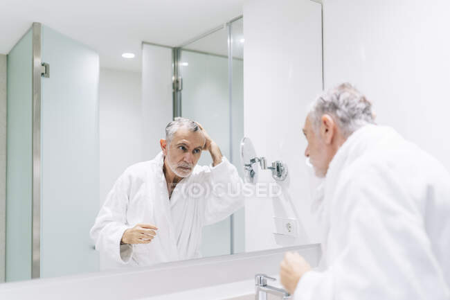 Bonito homem olhando para a reflexão no espelho do banheiro do hotel — Fotografia de Stock