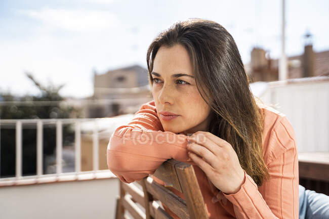 Mujer pensativa mirando hacia otro lado mientras está sentada en la azotea en un día soleado - foto de stock