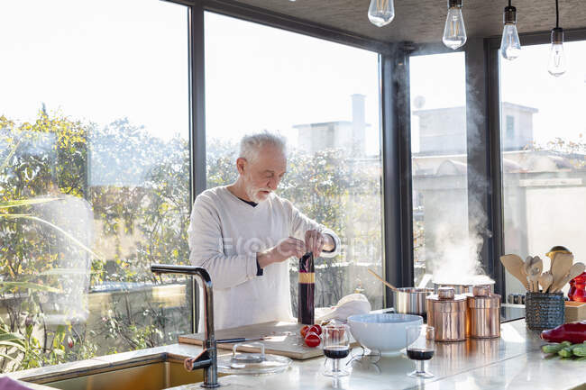 Homme âgé travaillant debout dans la cuisine à la maison — Photo de stock