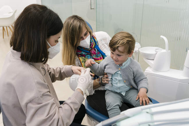 Dentista vestindo máscara protetora sentado por mulher e menino na clínica — Fotografia de Stock