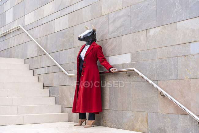 Donna con cappotto rosso e maschera di toro che tiene ringhiera mentre in piedi vicino alle scale — Foto stock