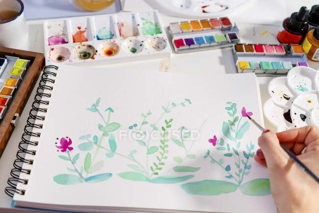 Mujer pintando plantas botánicas y flores sobre papel en la mesa - foto de stock
