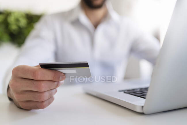 Entrepreneur with laptop holding credit card while sitting at desk in office — Stock Photo