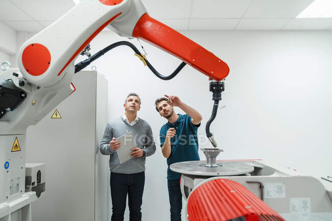Молодой инженер указывает на машины во время обсуждения со зрелым предпринимателем на заводе — стоковое фото