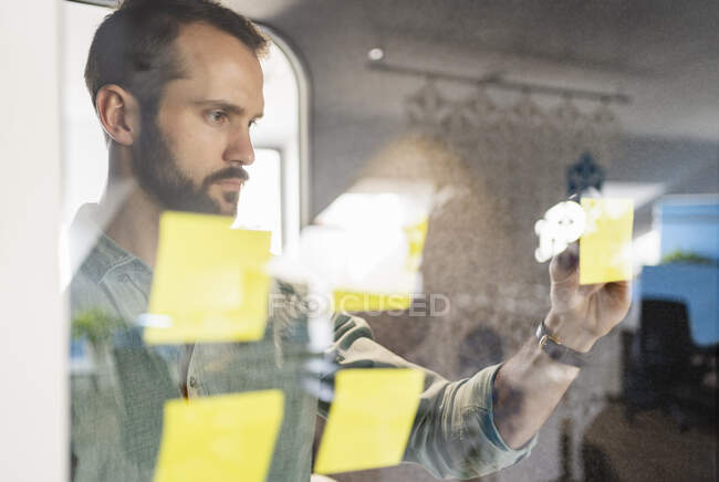 Молодой предприниматель пишет на клейкой ноте в офисе — стоковое фото