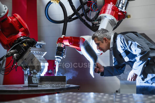Mature worker with welding helmet working at robotics in factory — Stock Photo