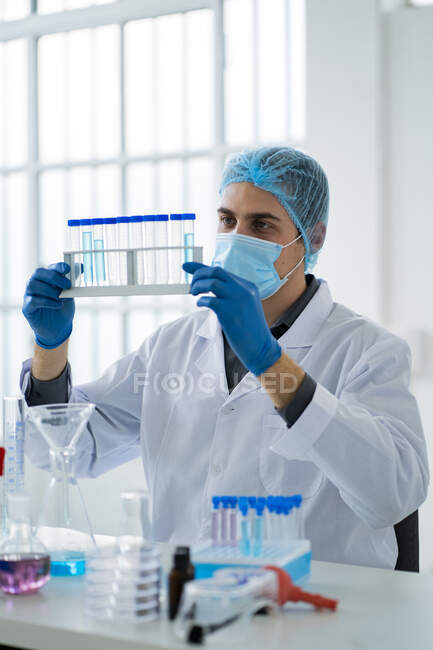 Científico masculino sosteniendo estante de tubo de ensayo en laboratorio durante COVID-19 - foto de stock
