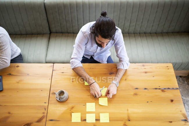 Empresario pegando nota adhesiva en la mesa mientras trabaja en la oficina - foto de stock