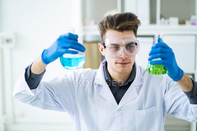 Científico masculino sosteniendo frascos químicos en laboratorio - foto de stock