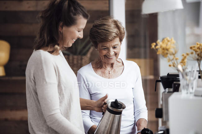 Sorridente giovane donna che tiene il bollitore dalla nonna a casa — Foto stock