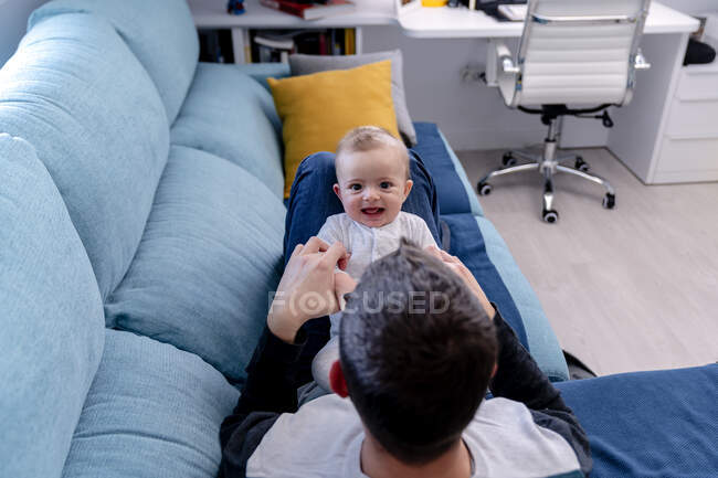 Батько грає гарного усміхненого сина на дивані у вітальні. — стокове фото