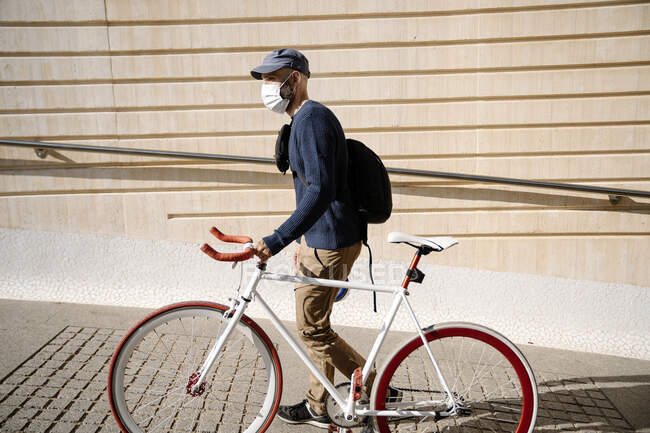 Homem com bicicleta olhando para longe enquanto caminhava pela parede no caminho durante o COVID-19 — Fotografia de Stock