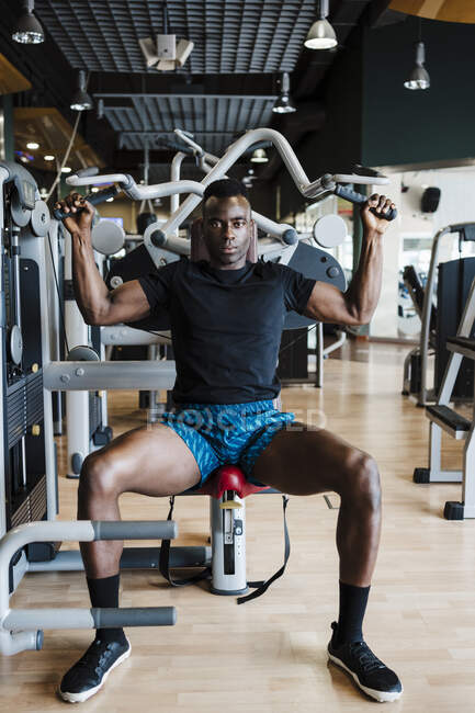 Atleta do sexo masculino sentado no equipamento de exercício no ginásio — Fotografia de Stock