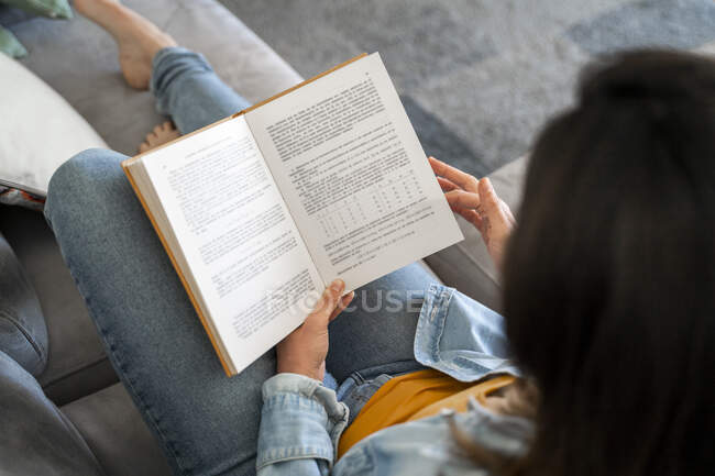 Жінка читає книгу, розслабляючись на дивані вдома — стокове фото