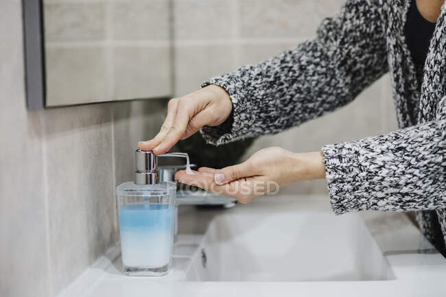 Woman spraying liquid soap in hand at sink in bathroom — Stock Photo