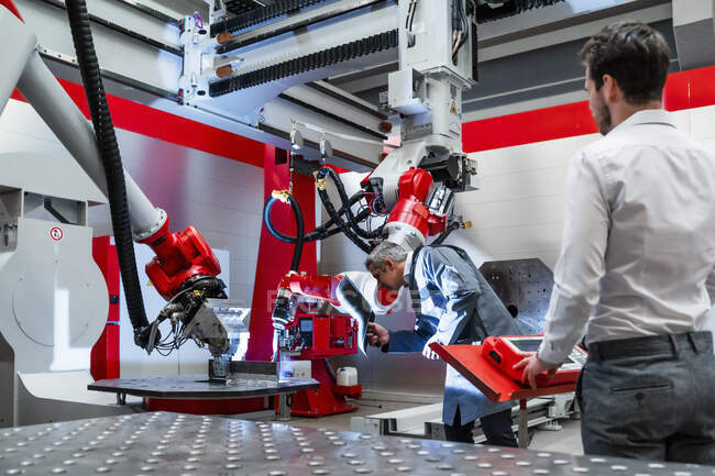 Зрелый инженер со сварочным шлемом работает на заводе по робототехнике — стоковое фото