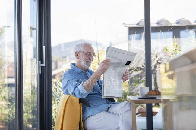 Чоловік читає газету, сидячи вдома. — стокове фото