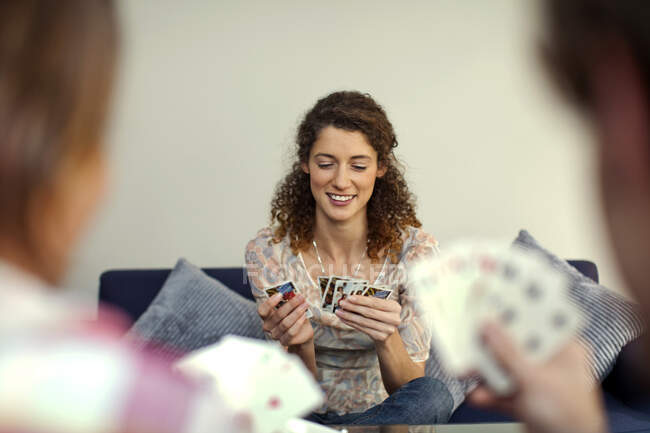 Hermosa mujer sonriendo mientras juega a las cartas con amigos - foto de stock
