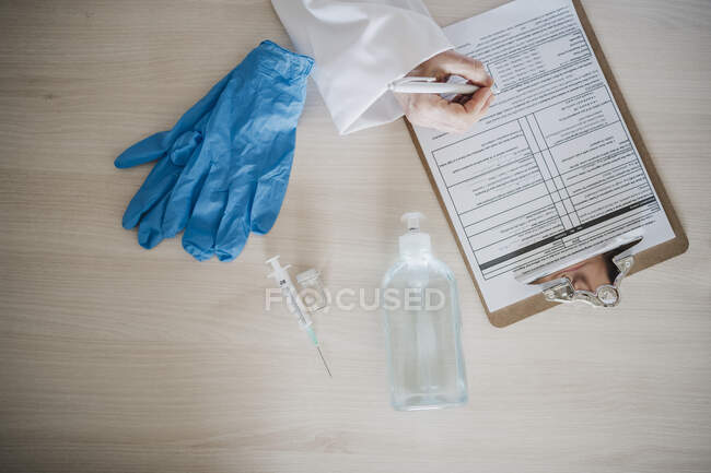 Female doctor writing on report on clipboard by medical equipment at desk — Stock Photo