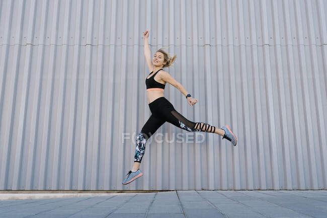 Atleta femenina despreocupada saltando por la pared durante el entrenamiento deportivo - foto de stock