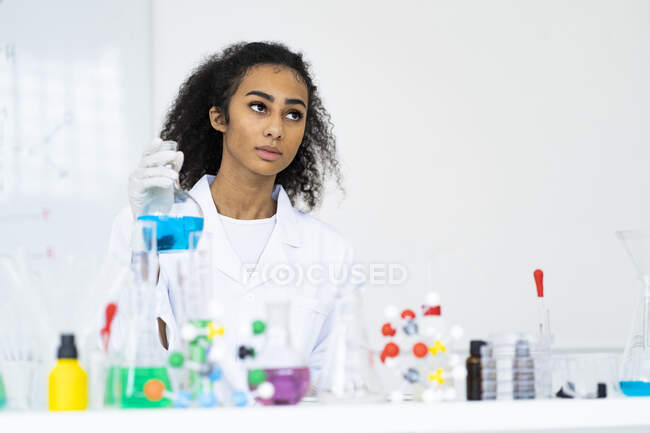 Investigadora reflexiva sosteniendo matraz de laboratorio mientras trabaja en laboratorio - foto de stock