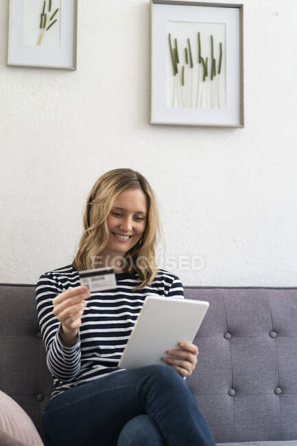 Woman using digital tablet while holding credit card at home — Stock Photo