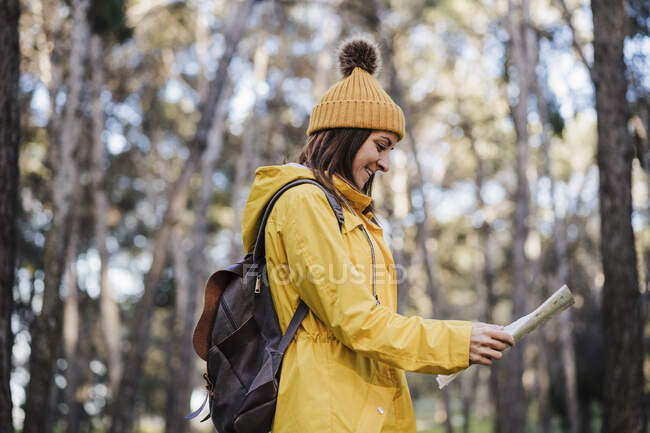Mujer sonriente leyendo mapa mientras explora en el bosque - foto de stock