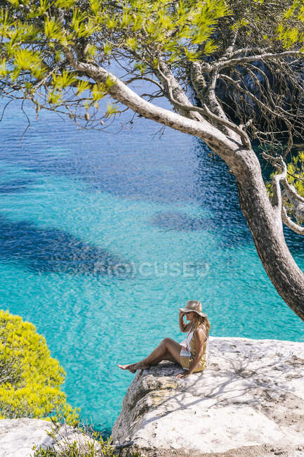 Зрелая женщина проводит свободное время, сидя на скале у моря — стоковое фото
