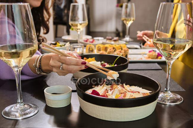 Donna che mangia con le bacchette mentre è seduta con gli amici al ristorante — Foto stock