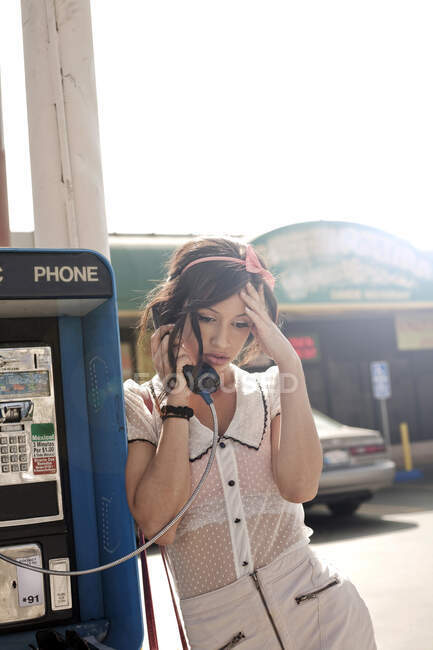 Worried woman with head in hand talking on pay phone at street during sunny day — Stock Photo