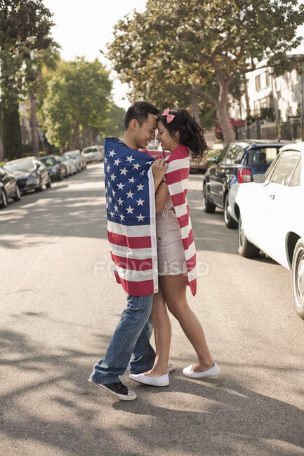 Girlfriend and boyfriend wrapped in American flag standing face to face on street in city — Stock Photo